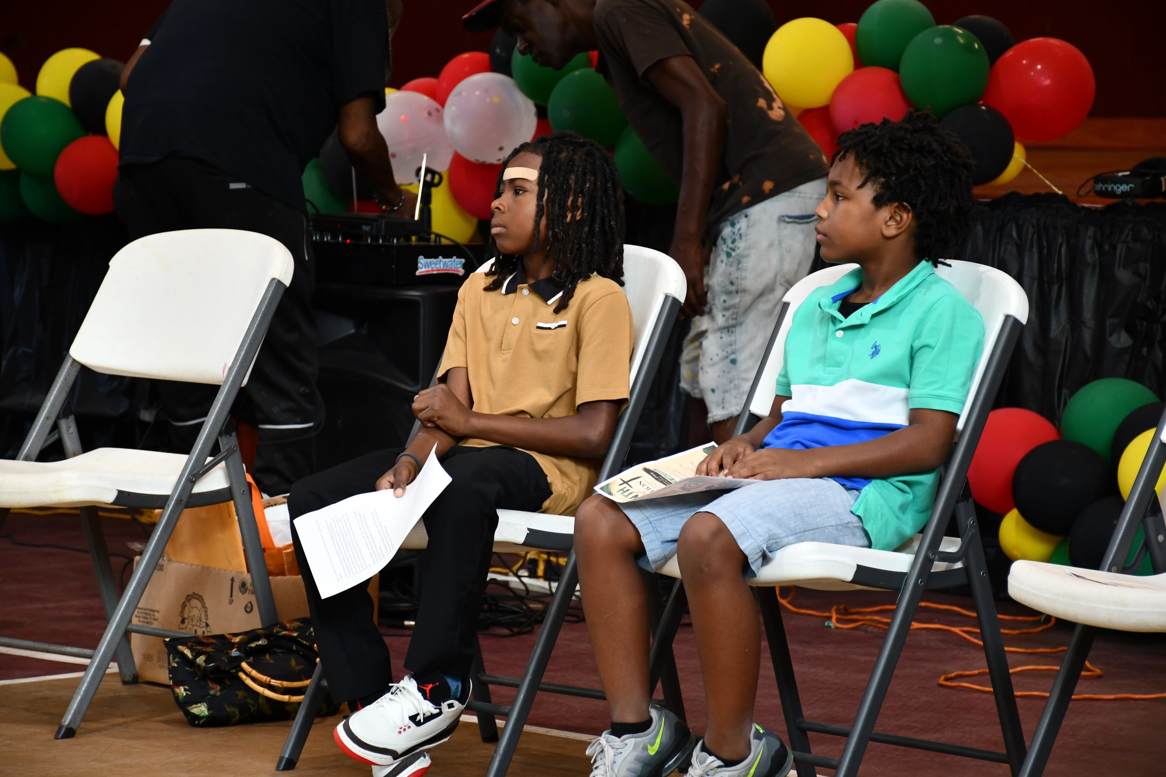 Two young boys seated with programs in front of a red, green, and yellow balloon arch at the Juneteenth gospel celebration