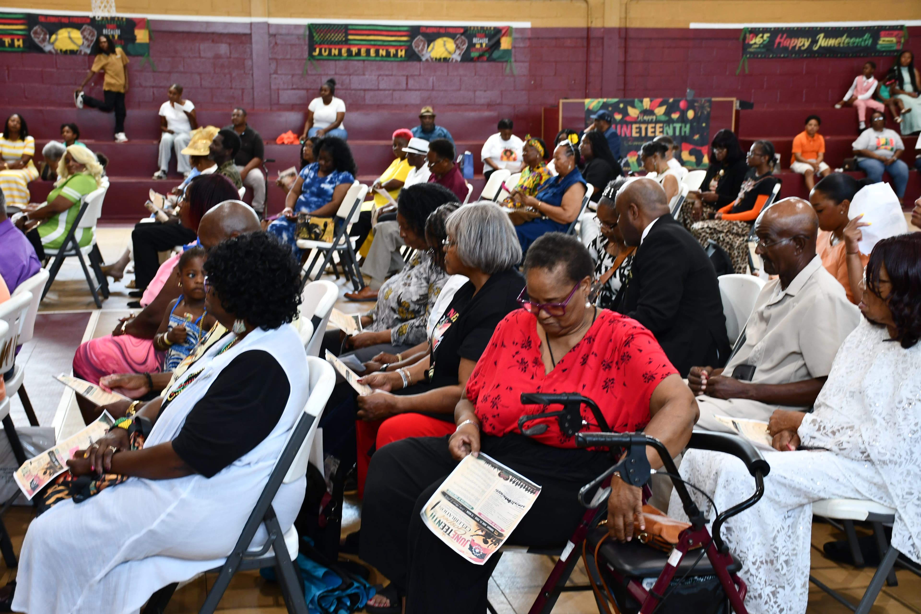 Audience seated with programs beneath Juneteenth banners in the Washington High School gymnasium