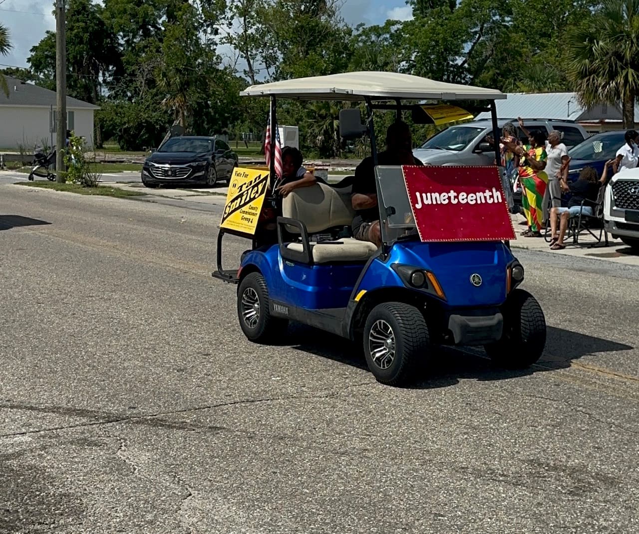 Golf cart with a Juneteenth sign riding through the parade route as spectators look on